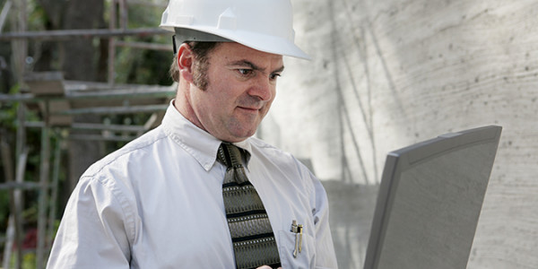 a construction engineer wearing a white helmet and holding a laptop